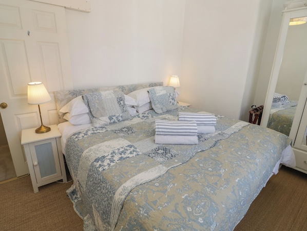 A neatly made bed with a patterned bedspread, two bedside lamps, and a small bedside table with a lamp. - Heath Cottage (Stratford-upon-Avon)