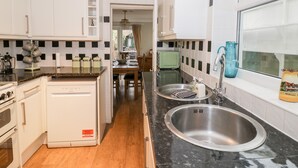 Una cocina compacta con armarios blancos, lavavajillas integrado, un lavabo y una ventana con vistas.