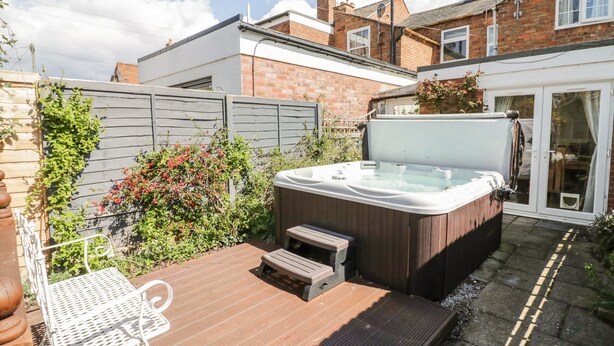 Un jacuzzi en una terraza de madera con una silla de metal, rodeado por una casa de ladrillo y una valla de madera.