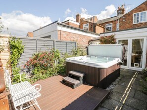 A hot tub on a wooden deck with a metal chair, surrounded by a brick house and a wooden fence. - Heath Cottage (Stratford-upon-Avon)