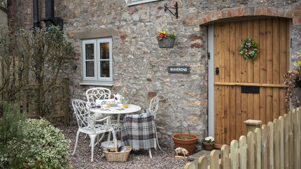 Un bâtiment en pierre avec une porte en bois, une enseigne indiquant « Waverly », et un petit jardin avec une table et des chaises.