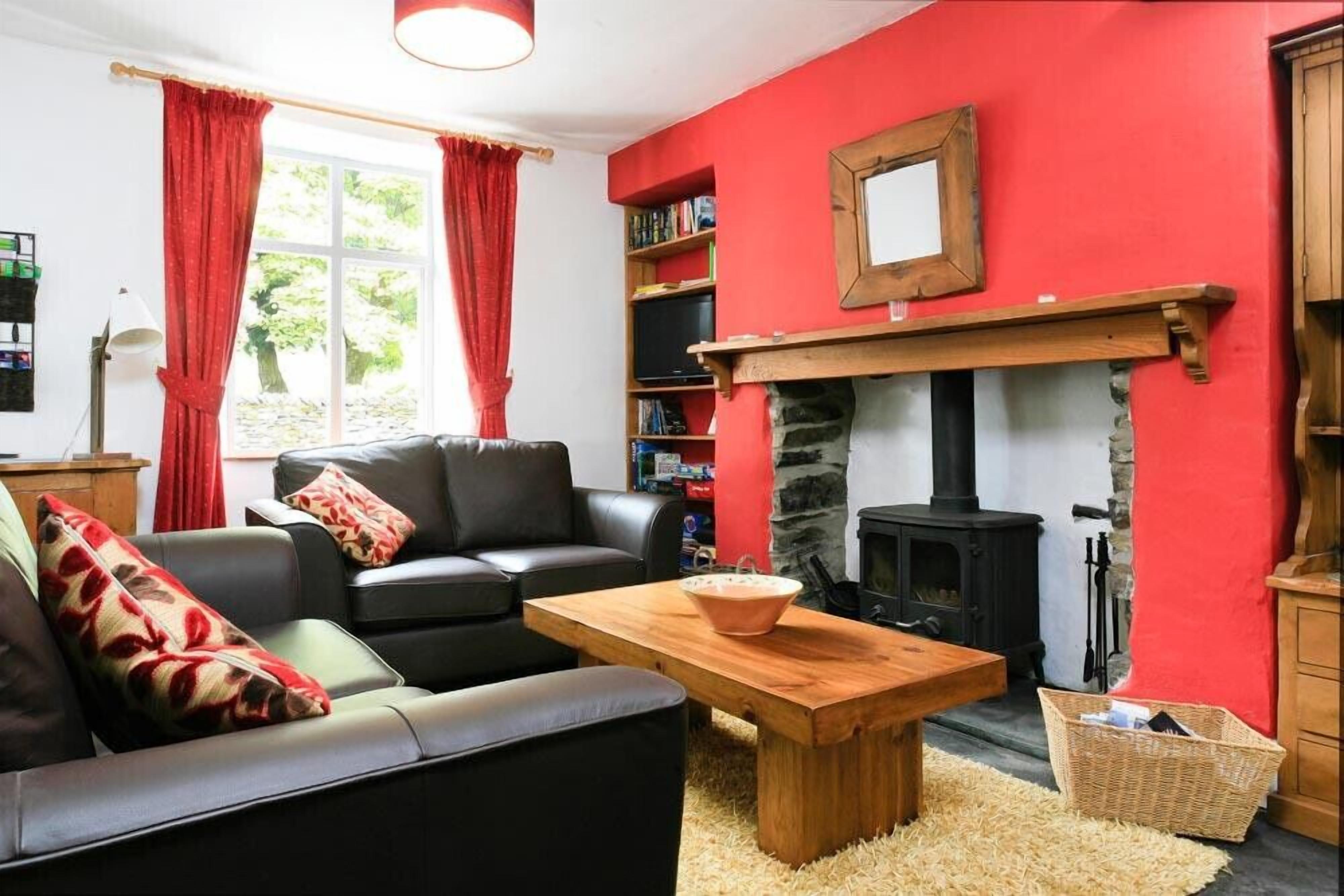 A cozy living room with a fireplace, red walls, a black sofa, and a wooden coffee table.