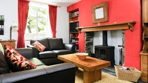 A cozy living room with a fireplace, red walls, a black sofa, and a wooden coffee table. - Stone Cottage at Staveley (Kendal)