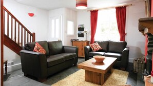 A living room with two black leather sofas, a wooden coffee table, a red-framed lamp, and a fireplace. - Stone Cottage at Staveley (Kendal)