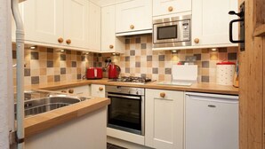 A compact kitchen with white cabinets, a microwave, a stove, and a dishwasher. - Stone Cottage at Staveley (Kendal)