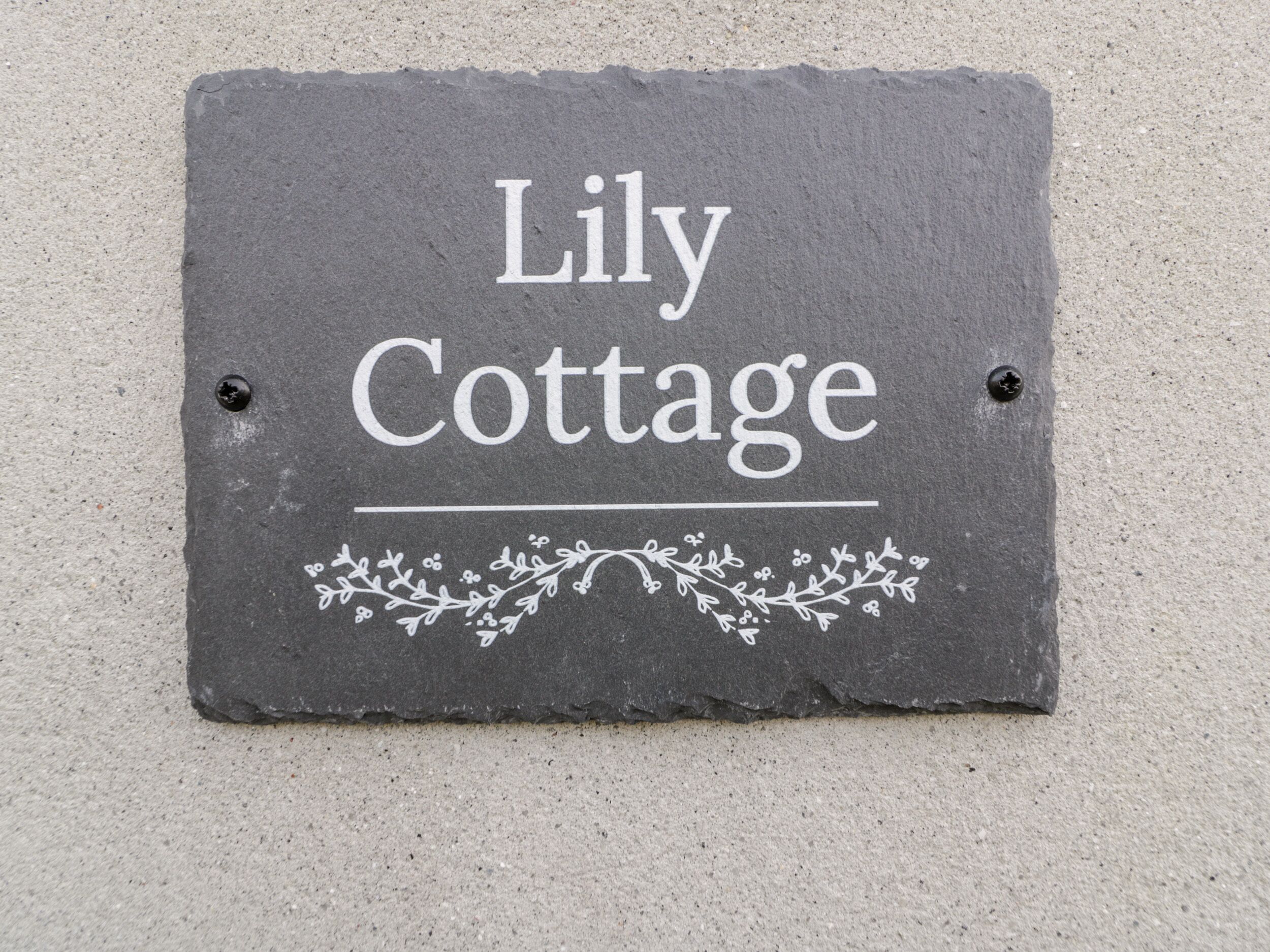 Un segnale in ardesia con la scritta "Lily Cottage", impreziosito da un decorativo motivo floreale sotto il testo.