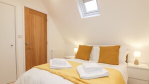 A bedroom with a bed, a nightstand, a window, and a door. - Lily Cottage (Camelford)