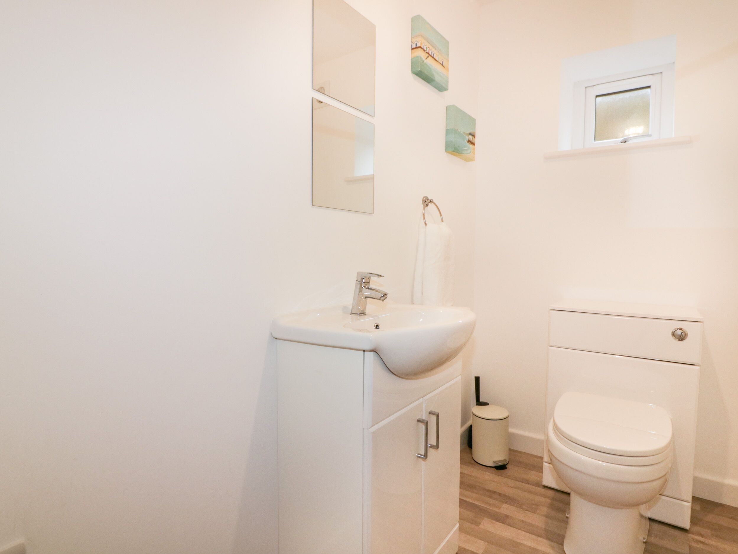 A bathroom with a white sink, mirror, toilet, and a trash bin.