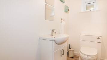A bathroom with a white sink, mirror, toilet, and a trash bin.