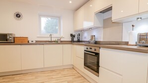 A modern kitchen with white cabinets, a wooden countertop, a built-in oven, and a microwave. - Lily Cottage (Camelford)