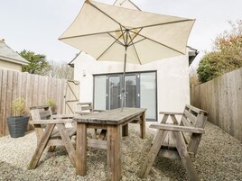 Un patio de madera con una mesa, sillas, un paraguas grande y una puerta corrediza de vidrio.