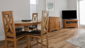 A dining area with a wooden table and chairs, a cabinet, a television, and a window with blinds.