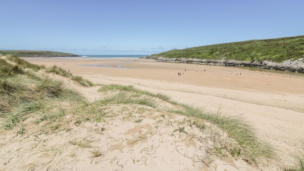 A wide sandy beach with gentle slopes and sparse vegetation.