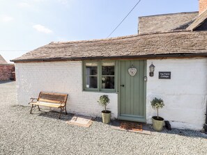 A white brick cottage with a green door, a bench outside, and a sign reading "Top Farm Cottage". - Top Farm Cottage (Oswestry)