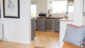 Una cocina moderna con lavavajillas, microondas y un lavamanos pequeño. Hay una obra de arte enmarcada en la pared y una ventana que proporciona luz natural.