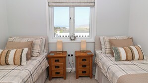 A twin bedroom with two beds, a window with a view, and a bedside table with a lamp. - Mcauliffe Lodge (Borth)