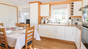 A modern kitchen with white cabinets, a wooden countertop, and a dining area with a table set for four. - Mcauliffe Lodge (Borth)