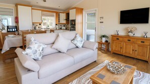 A modern living room with a sofa, wooden coffee table, and a television. - Mcauliffe Lodge (Borth)