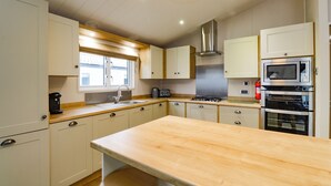 Een moderne keuken met witte kasten, een houten aanrecht, een roestvrijstalen afzuigkap, een magnetron en een oven.