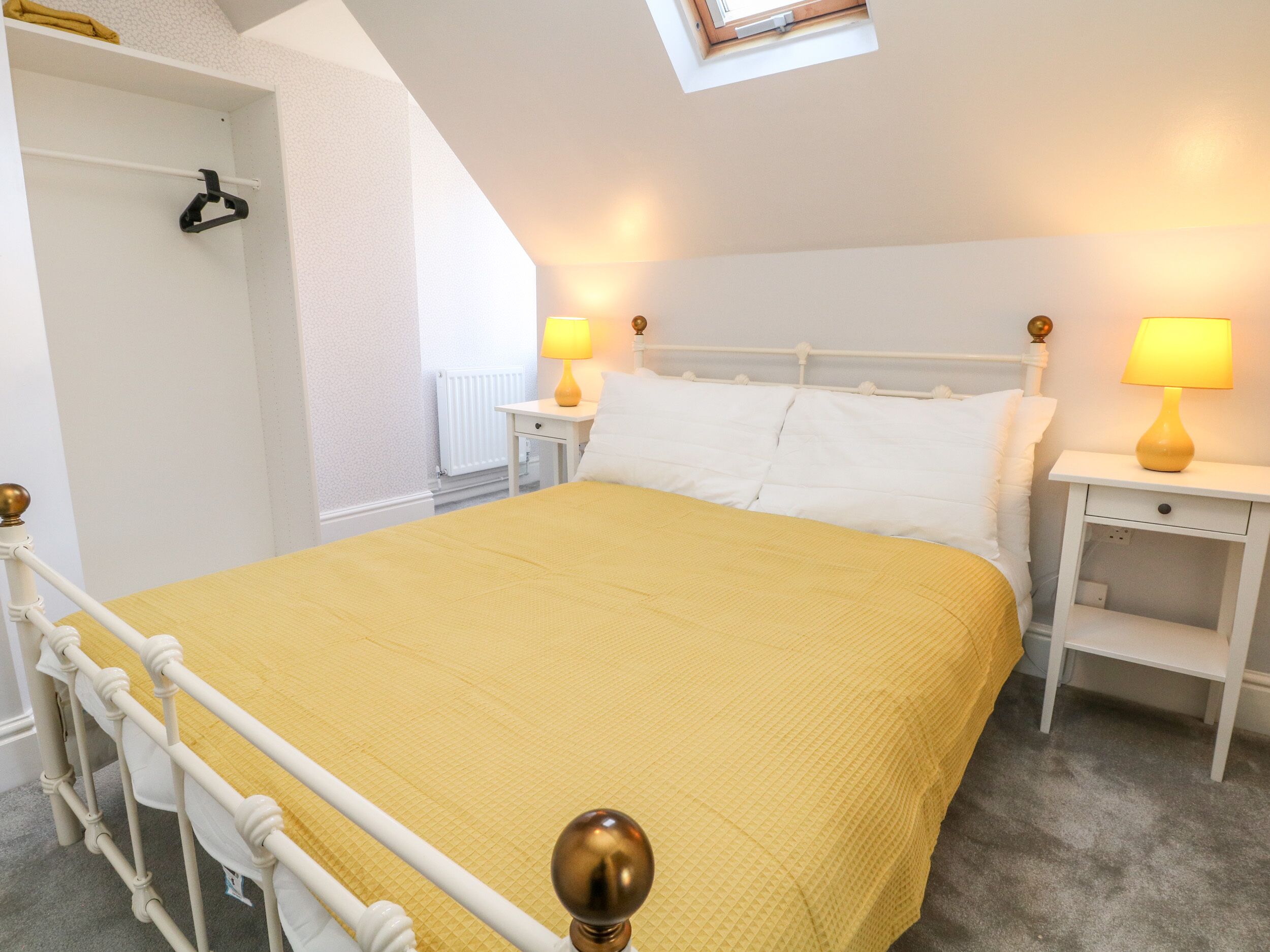 Una camera da letto ordinata con un letto, due comodini, un tavolo da notte, un termosifone e un armadio.
