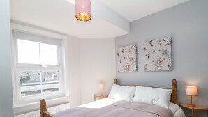 A bedroom with a wooden bed, white bedding, two bedside lamps, and floral artwork on the wall. - Arlington House (Matlock)