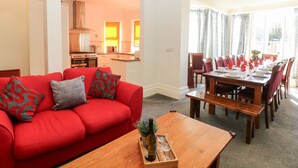 A modern living room with a red sofa, wooden coffee table, and a dining area with a large table and chairs. - Arlington House (Matlock)