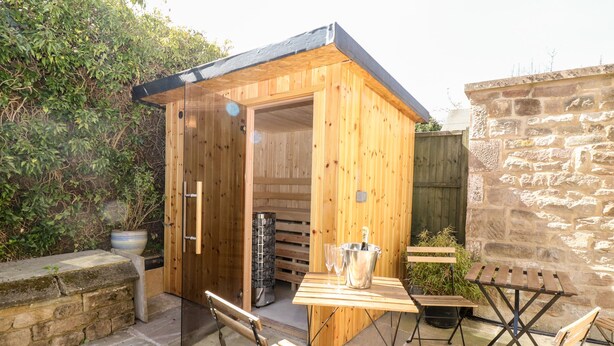 A wooden outdoor structure with a door, a table with chairs, and a potted plant. - Arlington House (Matlock)