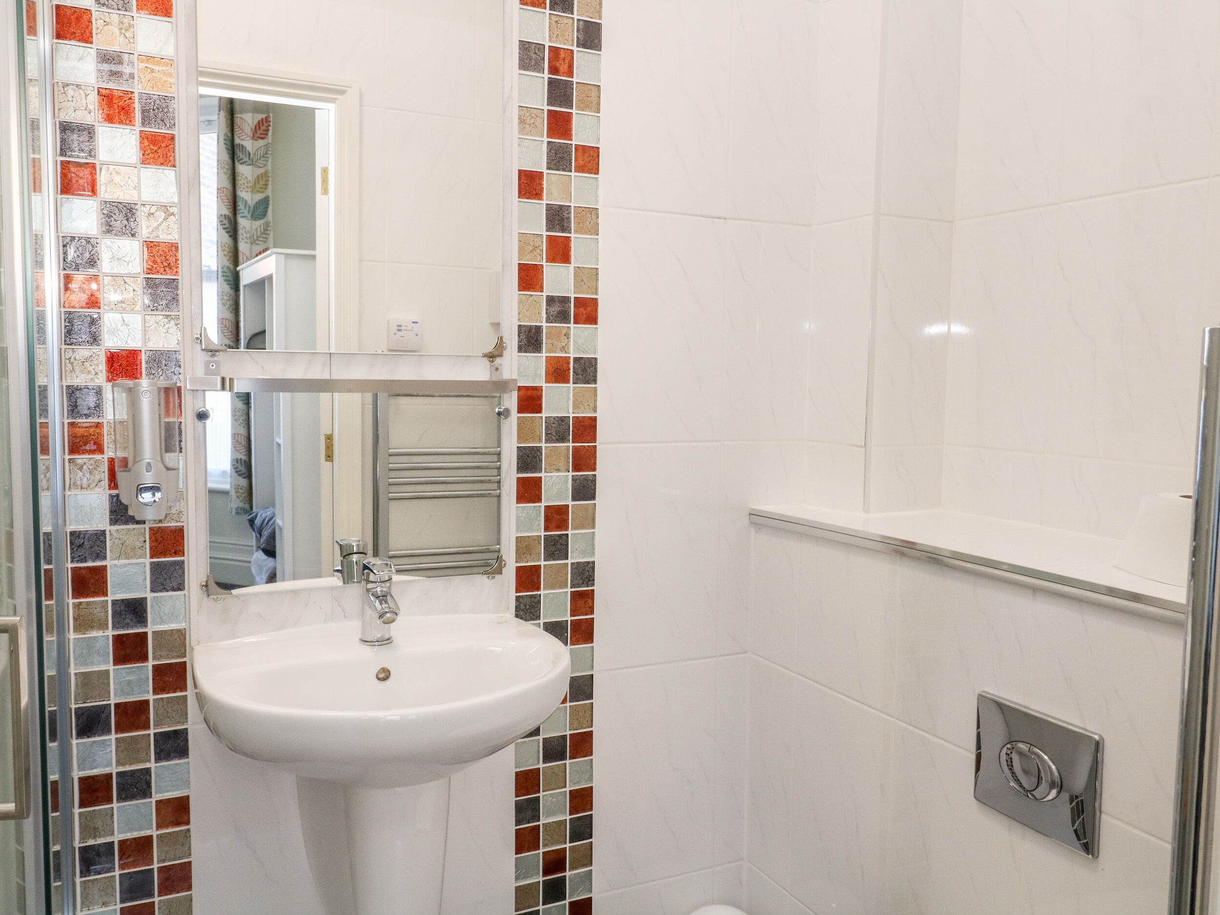 Un baño con lavamanos blanco, espejo y zona de ducha.