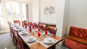 A dining area with a long wooden table set for six, red napkins, white plates, and wine glasses. There is a red upholstered bench to the right and a decorative wall piece above the table. - Arlington House (Matlock)