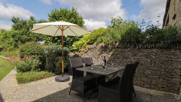 Eine Terrasse im Freien mit Tisch, Stühlen und einem großen Sonnenschirm, sowie einer Steinmauer.