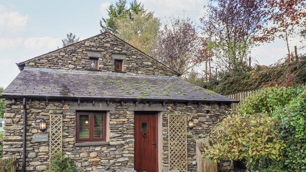 A stone cottage with a wooden fence, a sign indicating private parking, and a sign reading "Millrace Cottage". - Millrace Cottage (Kendal)