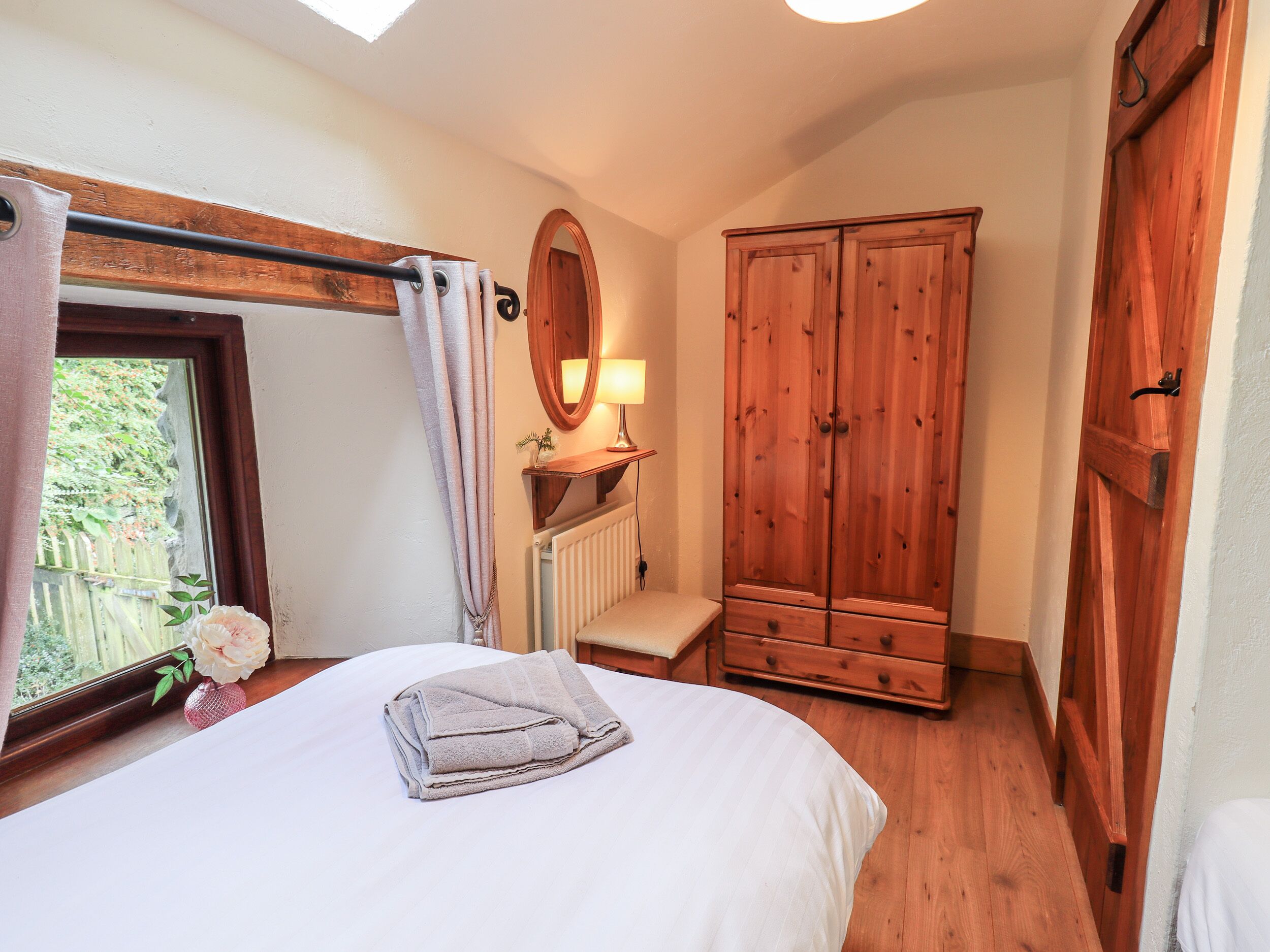A bedroom with a bed, a wooden wardrobe, a radiator, and a window with curtains.