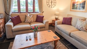A cozy living room with two sofas, a wooden coffee table, and a clock on the wall. - Millrace Cottage (Kendal)