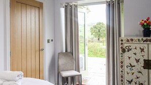 Une chambre d’hôtel avec une porte en bois, une chaise, un lit recouvert d’une couette blanche et un meuble orné de motifs floraux.