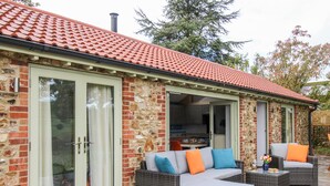 Une maison avec une façade en pierre, un toit en tuiles et une terrasse aménagée avec des meubles et des coussins en osier.