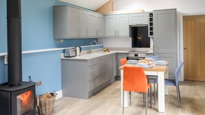 Une cuisine moderne avec des meubles gris, une cuisinière noire et un coin repas avec des chaises orange.