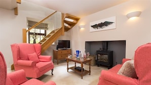 A living room with a wooden staircase, a fireplace, and two pink armchairs. - Barn Cottage (Cockermouth)
