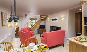 A cozy living room with a staircase, a dining area with a fruit bowl, and a kitchen counter with a cutting board. - Barn Cottage (Cockermouth)