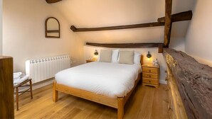 A bedroom with a wooden bed, a nightstand with a lamp, a radiator, and a wooden chair. - Barn Cottage (Cockermouth)