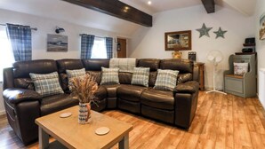 Un salon avec un canapé d’angle, une table basse en bois et un ventilateur.