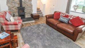 A cozy living room with a stone wall, a fireplace, a brown leather sofa, a plaid armchair, and a wooden coffee table. - Y Beudy (Crymych)