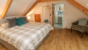 A bedroom with a sloped ceiling, a bed with plaid bedding, a chair, and a small bathroom with a mirror and sink. - Y Beudy (Crymych)