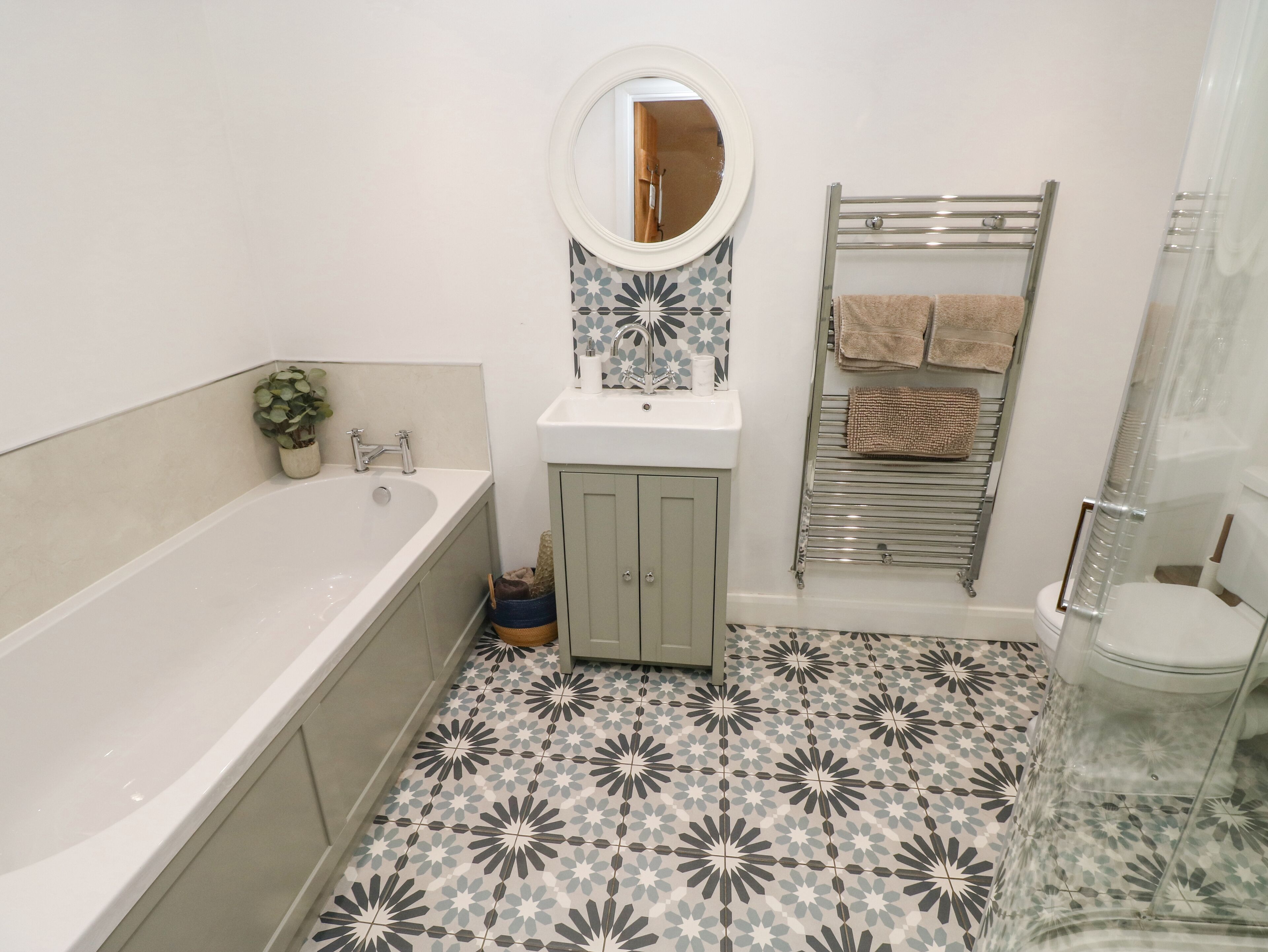 A bathroom with a bathtub, a sink with a mirror, a towel rack, and patterned floor tiles.