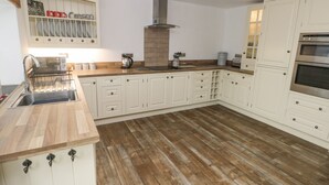 A modern kitchen with white cabinetry, a wooden countertop, and a stainless steel sink. - Y Beudy (Crymych)