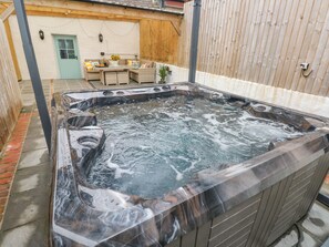 Un bain à remous avec un revêtement extérieur en bois, un espace patio avec une table et des chaises, et une clôture en bois en arrière-plan.