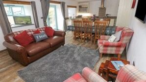 A living room with a brown leather sofa, plaid armchairs, a grey rug, and a dining table with chairs. - Y Beudy (Crymych)