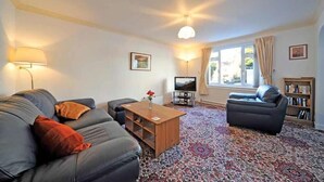 A living room with a sofa, a coffee table, a television, and a bookshelf. - Mosslea (Windermere)