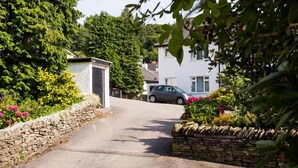 A residential street with a stone wall, a parked car, and houses with white exteriors. - Mosslea (Windermere)