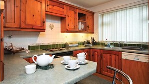A kitchen with wooden cabinets, a countertop with a kettle, cups, and a toaster. - Mosslea (Windermere)