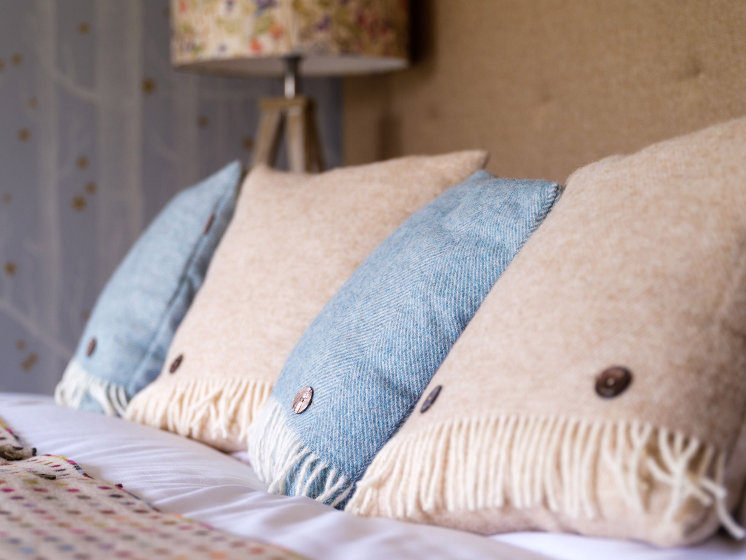 Una cama con dos almohadas, una color beige y otra de tela vaquera azul, cubierta con una colcha estampada.